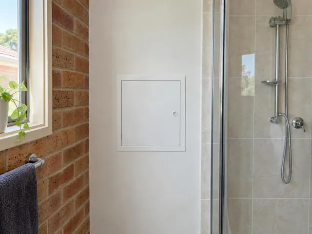 Neat access panel in a white bathroom wall beside a tiled shower in Valentine