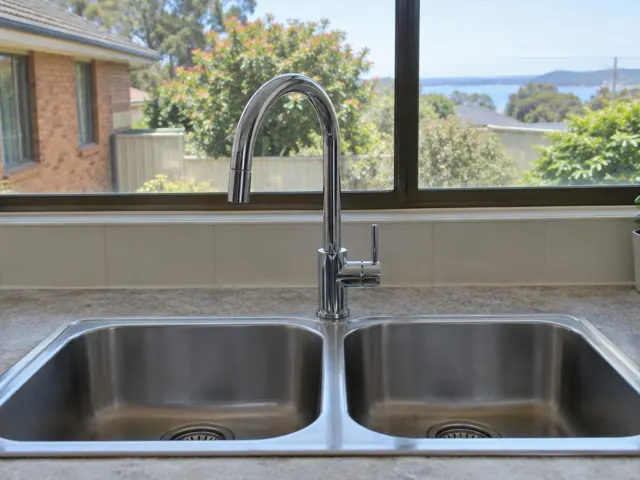 Chrome kitchen mixer tap over a double stainless steel sink with window view in Croudace Bay